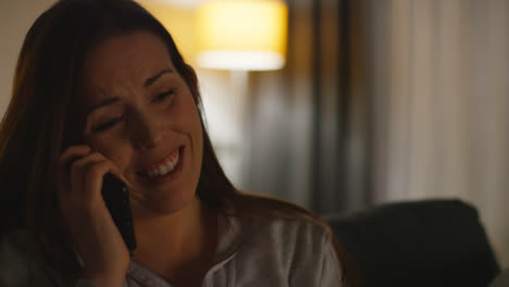 Close-Up-Of-Smiling-Woman-Sitting-On-Sofa-At-Home-At-Night-Talking-On-Mobile-Phone-Shot-In-Real-Time-1